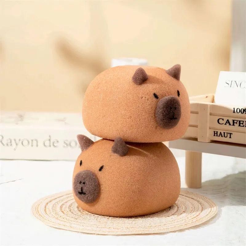 Stacked brown capybara-shaped sponges with dark ears and nose on woven mat and table.