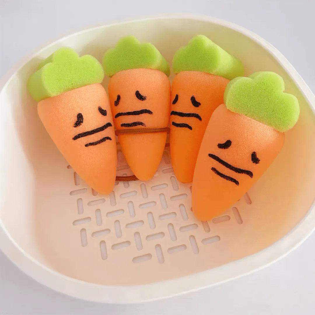 Four orange carrot-shaped sponges with green tops and sad faces placed in a white plastic basket.
