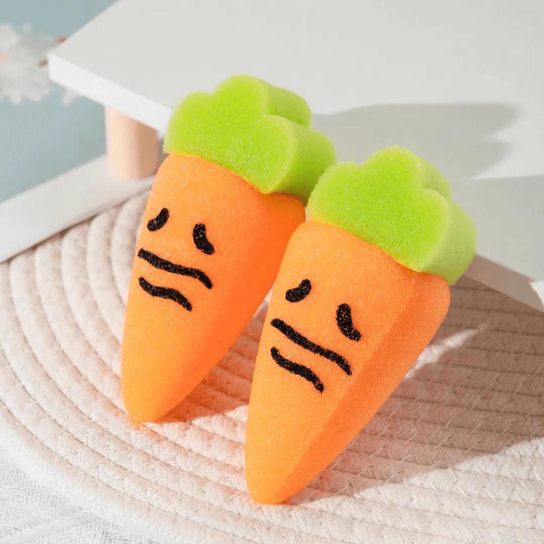 Two cute carrot-shaped orange sponges with green tops and sad faces on textured mat.