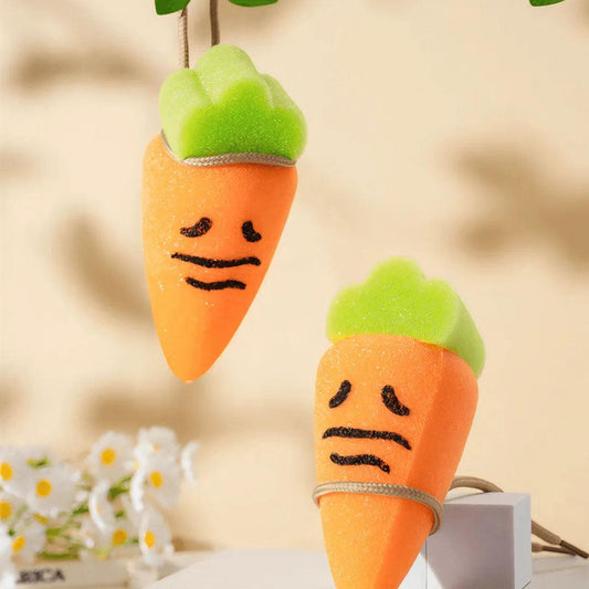 Two orange carrot-shaped sponges with green tops and sad faces, one hanging on beige wall.