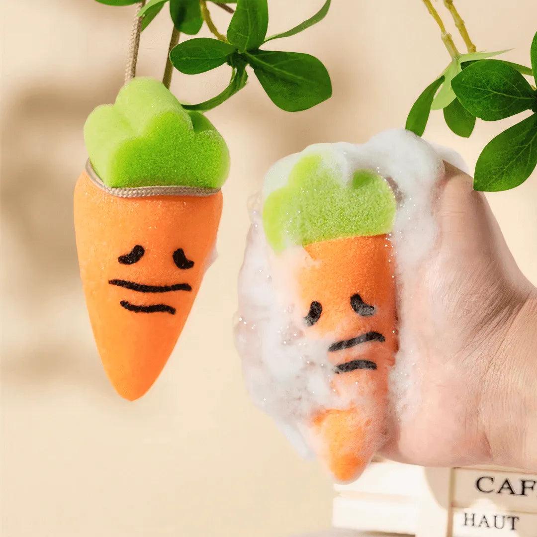 Orange carrot-shaped sponge with green top in hand covered in foam, another hanging beside it.