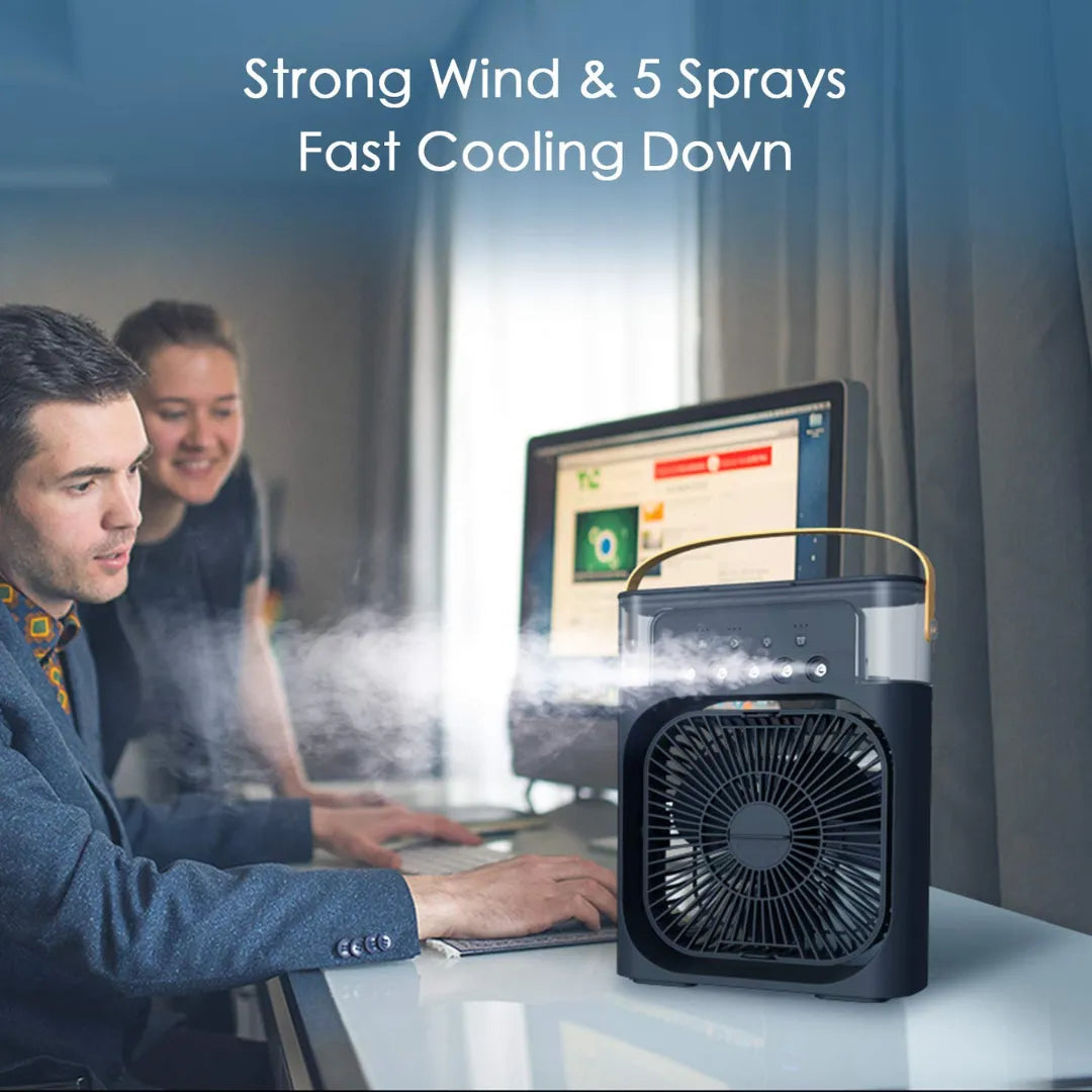 Black portable air cooler emitting strong mist with "Strong Wind & 5 Sprays Fast Cooling Down" text, placed on desk while two colleagues work in modern office.