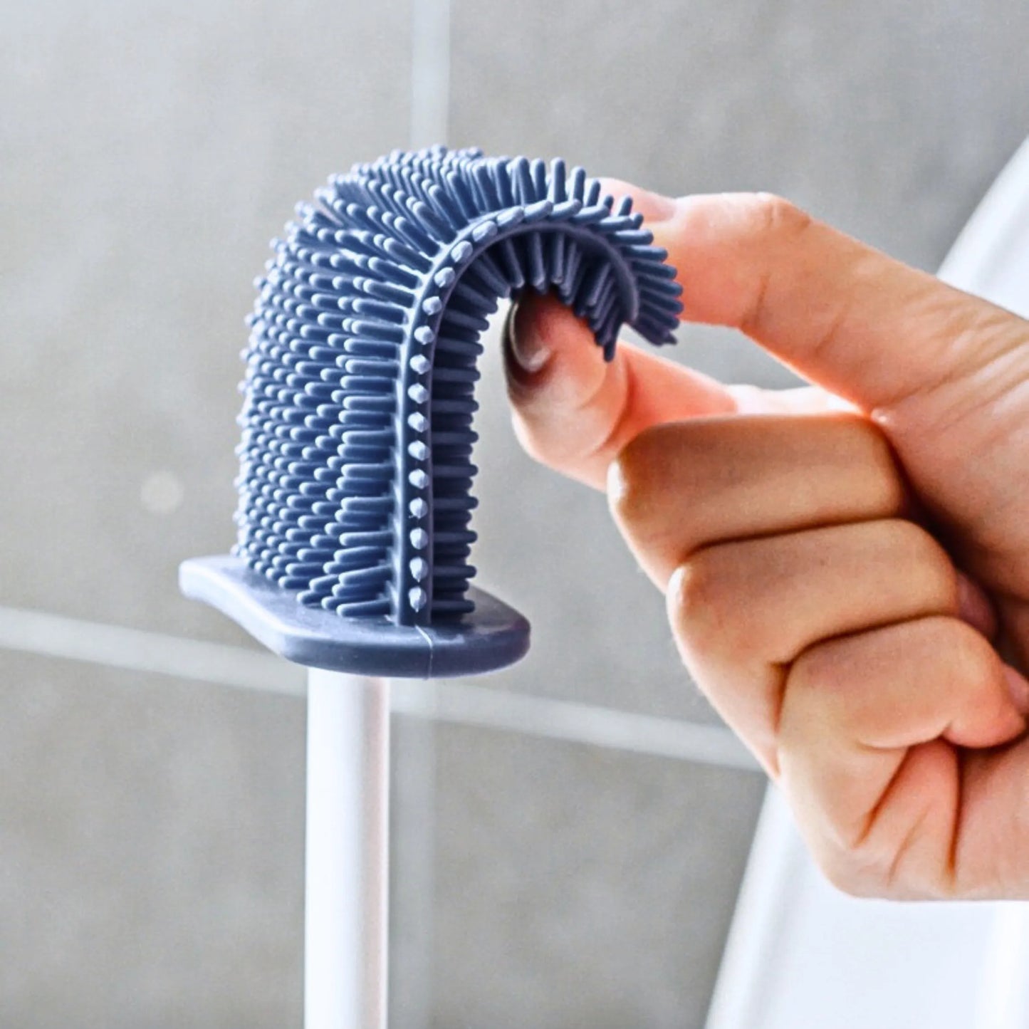 Close-up of a hand bending a D-shaped silicone toilet brush head, showing its soft, flexible design ideal for reaching all toilet corners without trapping dirt.