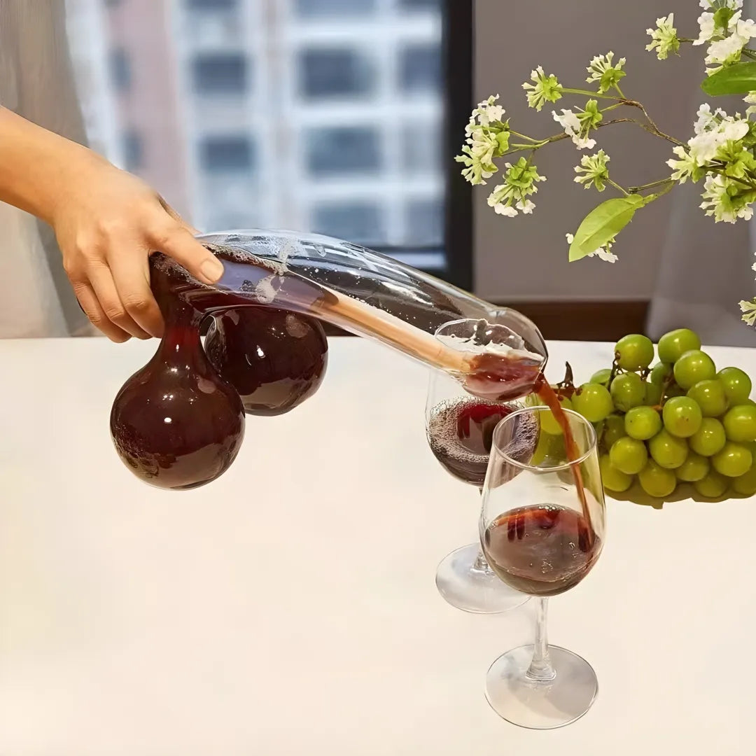 Person pouring red wine from a decanter into a glass with grapes and flowers on a table.