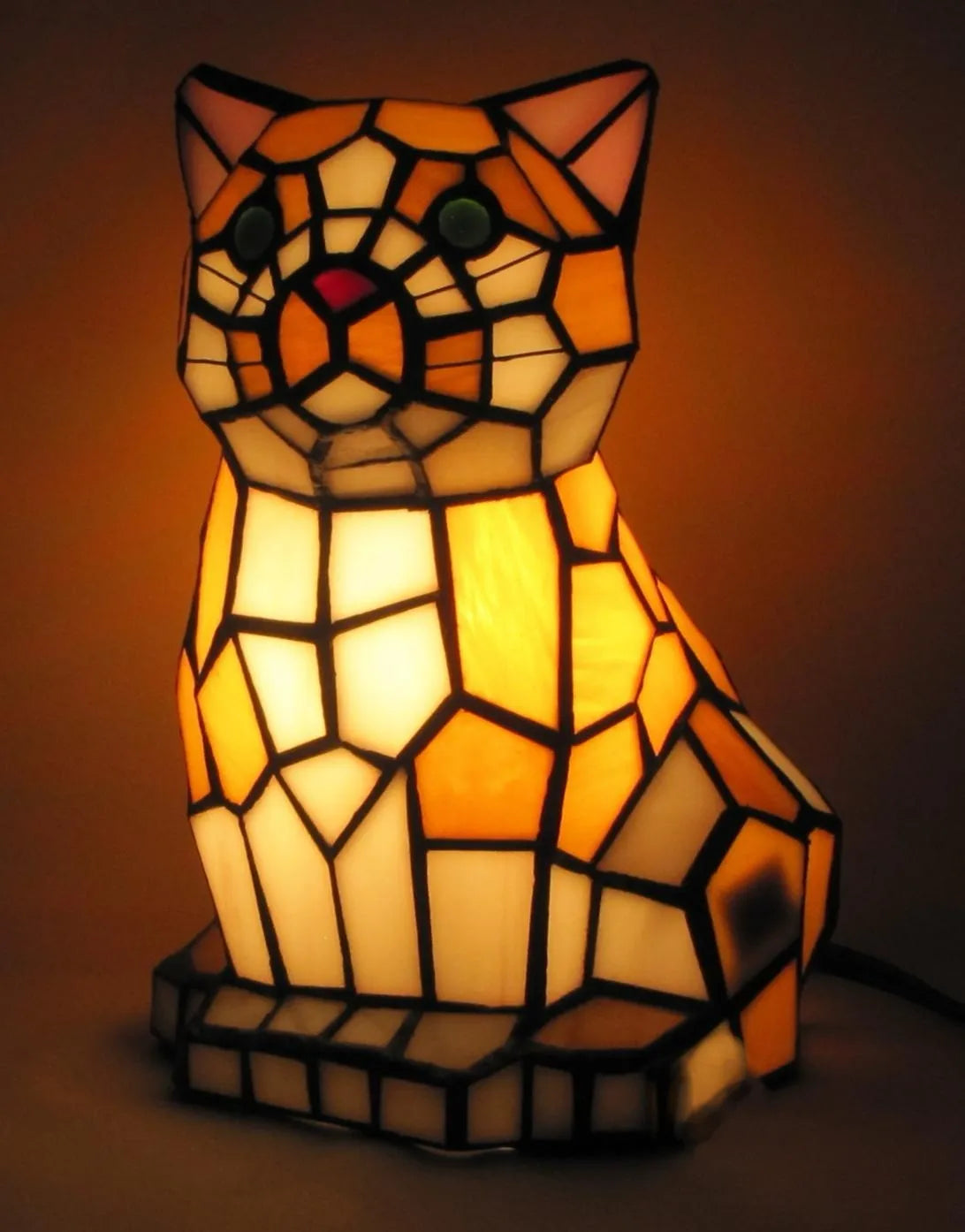 Stained glass cat-shaped lamp with warm glow on a dark background