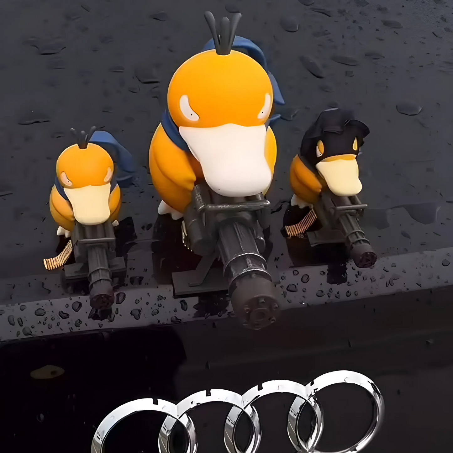 Three Psyduck car ornaments for Pokemon lovers mounted on glossy Audi surface, featuring unique outfits and toy guns with water droplet accents.