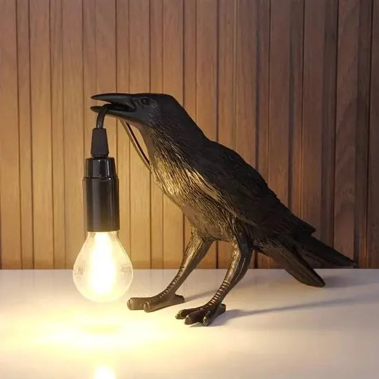Decorative lamp shaped like a crow with a light bulb in its mouth against a wooden background