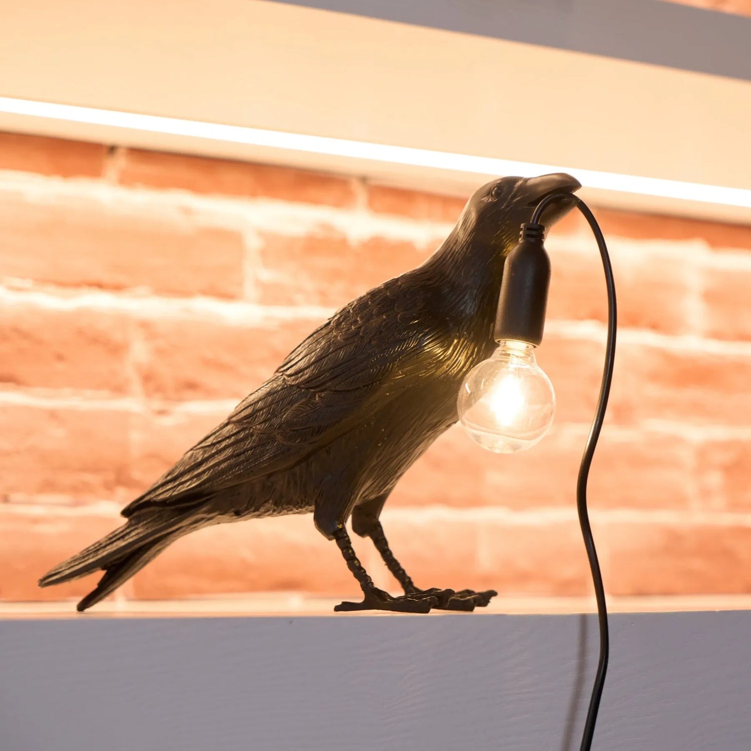 Bird-shaped lamp with a light bulb in front of a brick wall