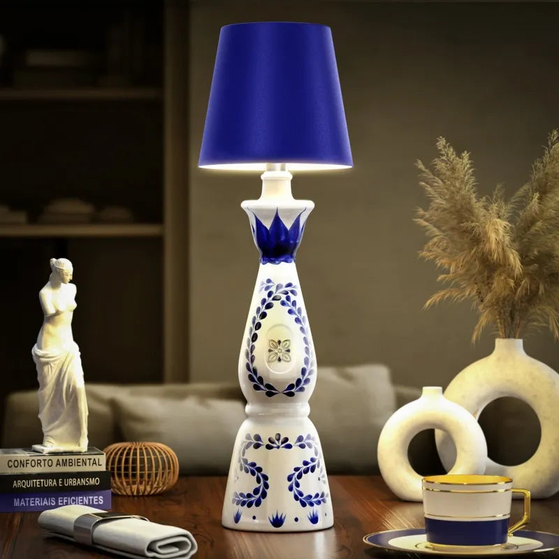 Decorative table lamp with blue shade on a wooden surface, surrounded by books and a cup.