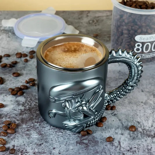 Metallic mug with dragon handle filled with coffee, surrounded by coffee beans on a textured surface.