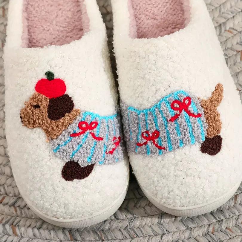 Close-up of a pair of white memory foam house shoes featuring a delicate embroidered dachshund pattern with red bows and blue stripes, on a textured rug.