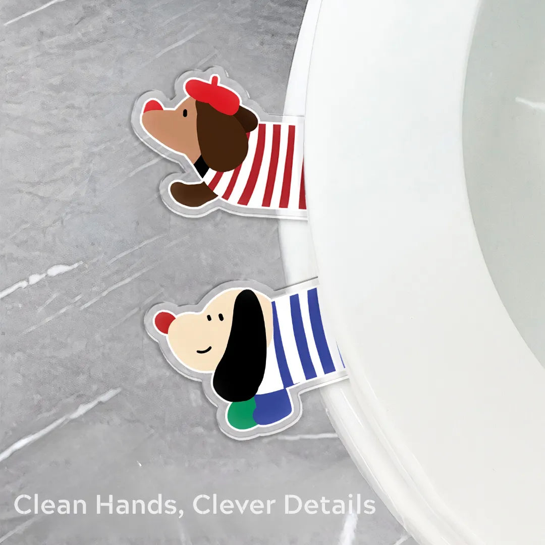 Two dachshund-shaped toilet seat lifters in red and blue striped outfits attached to the rim of a white toilet seat on a gray bathroom floor.