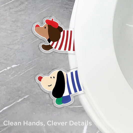 Two dachshund-shaped toilet seat lifters in red and blue striped outfits attached to the rim of a white toilet seat on a gray bathroom floor.