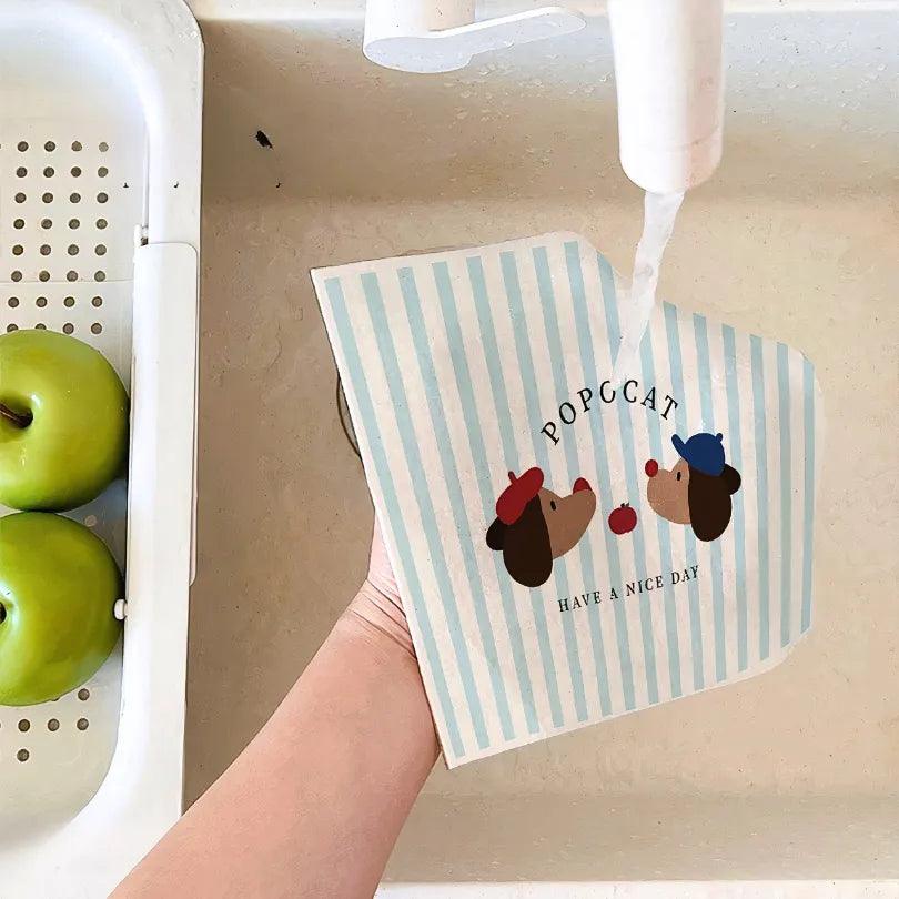 Rinsing dachshund-print cellulose towel under tap, showing strong absorbency and soft natural material.