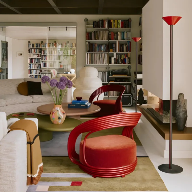 Modern living room with red chairs, a green rug, and bookshelves.