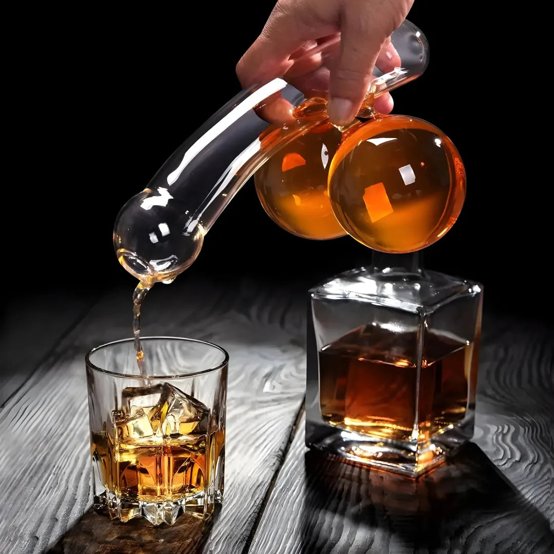 Hand pouring whiskey from a decanter into a glass with ice cubes on a wooden surface.
