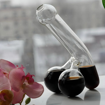 Funny decanter with dark liquid among pink orchids against cityscape. Humorous glassware for bar decor.