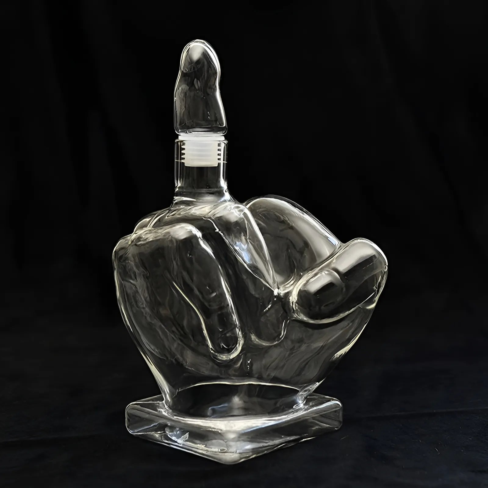 Clear glass middle finger decanter with stopper isolated on black background. Hand-shaped liquor bottle for whiskey or bar decor.