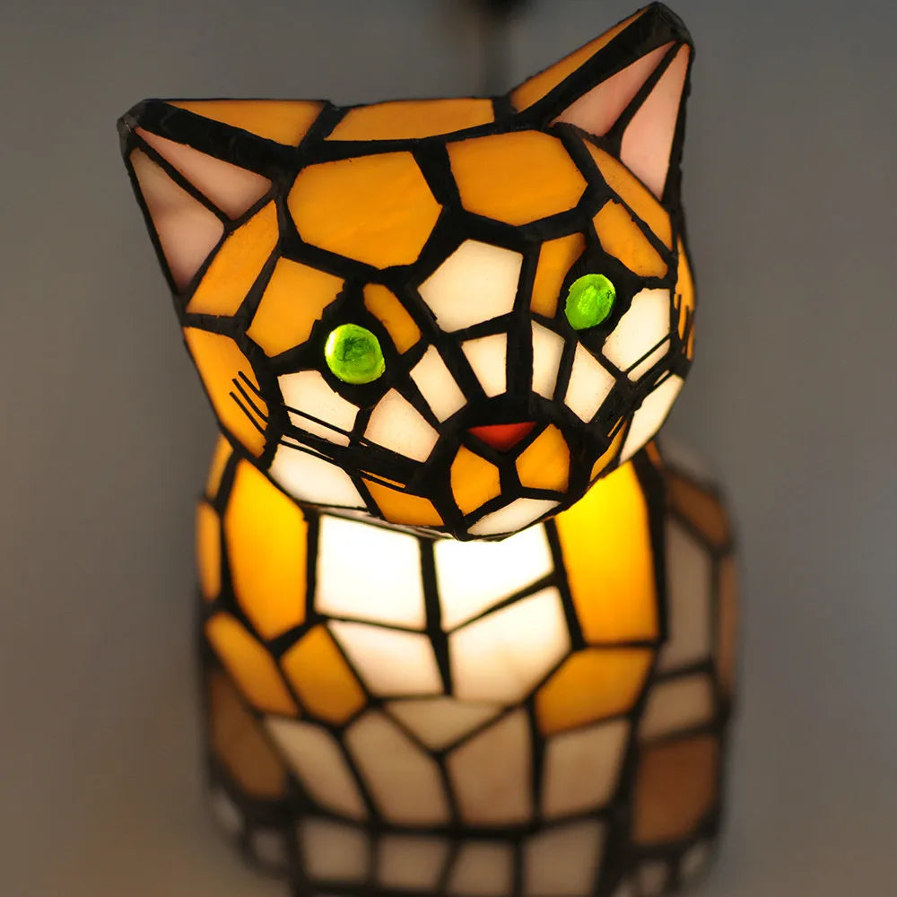 Stained glass cat-shaped lamp with a warm glow on a dark background