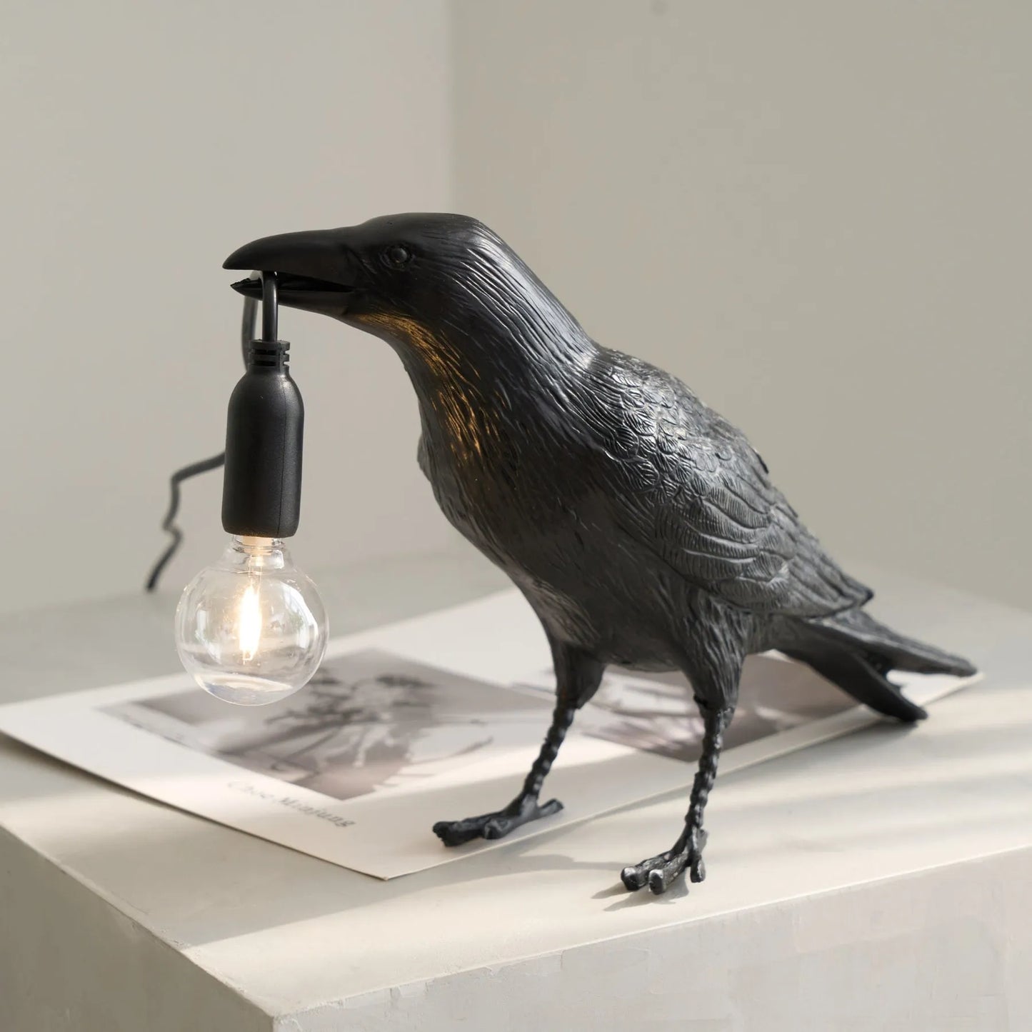 Black crow-shaped lamp with a light bulb on a neutral background