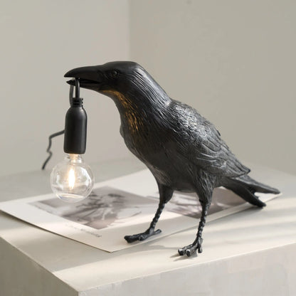 Black crow-shaped lamp with a light bulb on a neutral background