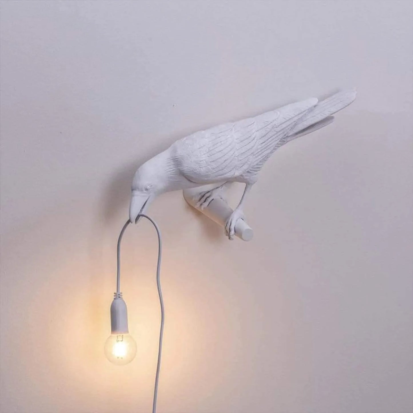 White bird-shaped wall lamp with a light bulb inside on a plain wall.