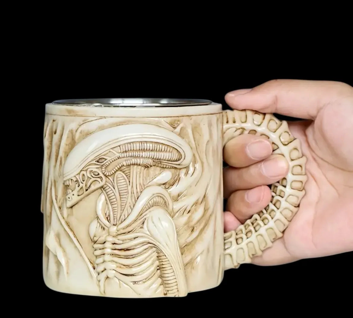 Hand holding a mug with detailed alien design against a black background